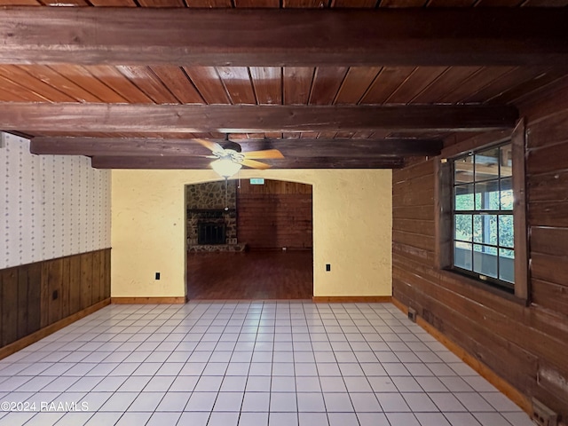 tiled spare room featuring ceiling fan, beam ceiling, wooden walls, wood ceiling, and a fireplace