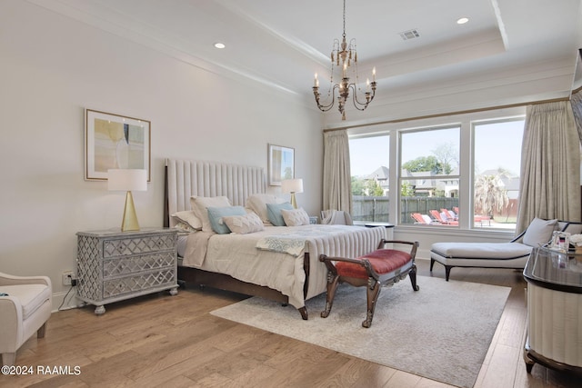 bedroom with a raised ceiling, hardwood / wood-style flooring, and a chandelier