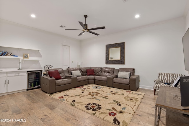 living room with beverage cooler, ceiling fan, light wood-type flooring, and ornamental molding