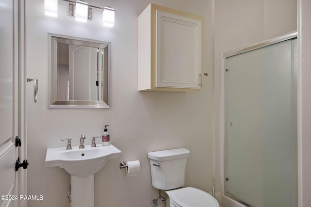 bathroom featuring a shower with door, sink, and toilet