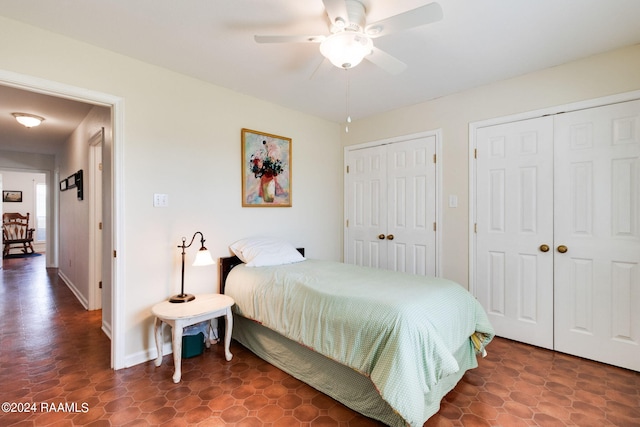 bedroom with tile flooring, ceiling fan, and two closets