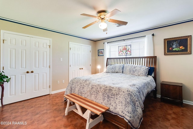 tiled bedroom with ornamental molding, ceiling fan, and two closets