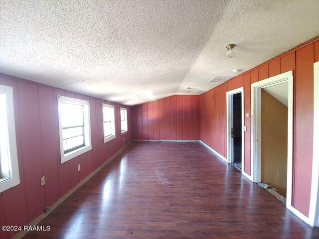 unfurnished room with dark wood-type flooring, vaulted ceiling, and a textured ceiling