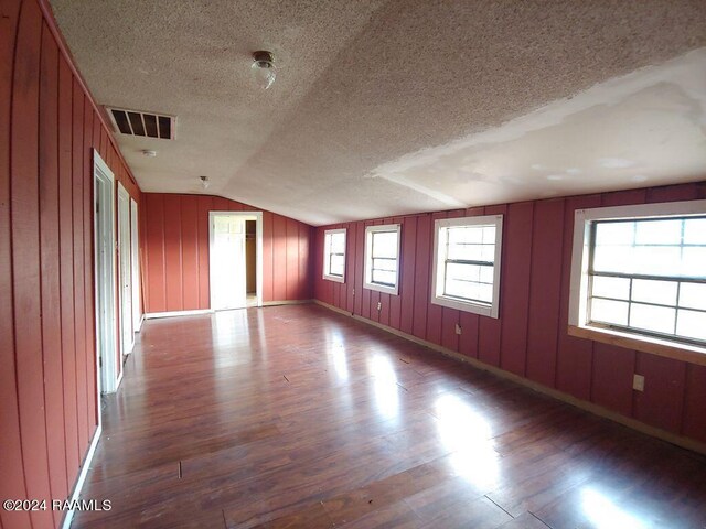 empty room featuring wood walls, hardwood / wood-style flooring, a textured ceiling, and vaulted ceiling