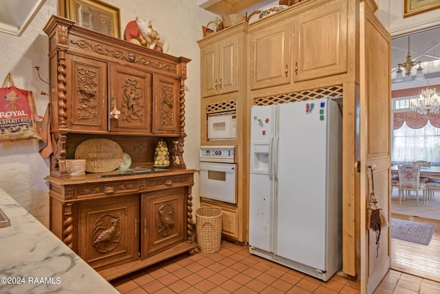 kitchen with a notable chandelier, white appliances, light tile floors, and light stone countertops