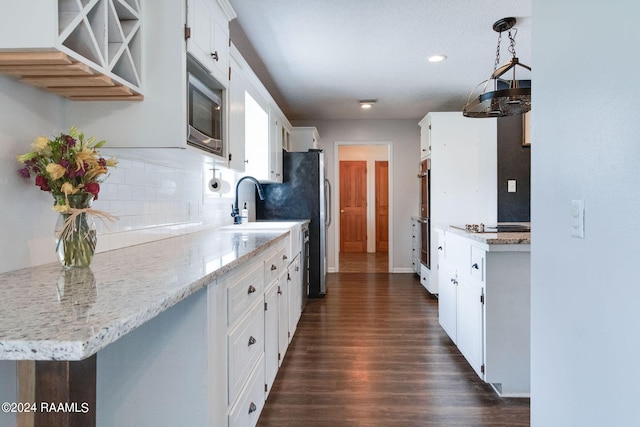 kitchen with pendant lighting, white cabinets, dark hardwood / wood-style floors, stainless steel microwave, and tasteful backsplash