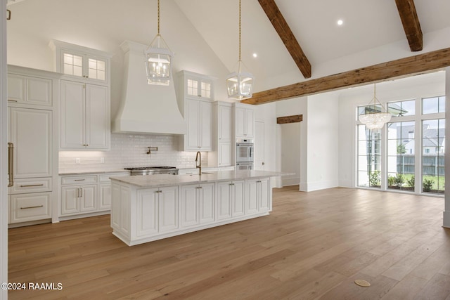 kitchen featuring high vaulted ceiling, an island with sink, white cabinets, and custom exhaust hood