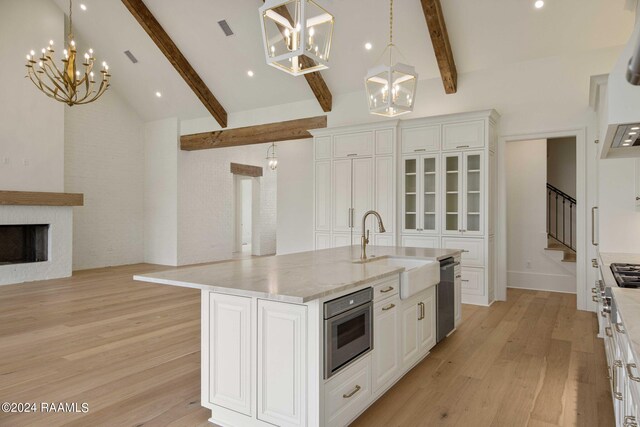 kitchen with dishwasher, a large fireplace, sink, beamed ceiling, and a kitchen island with sink