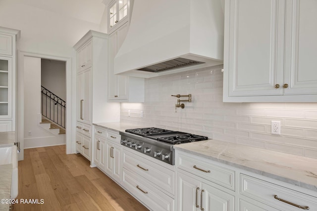 kitchen featuring light stone countertops, stainless steel gas stovetop, white cabinetry, and custom range hood