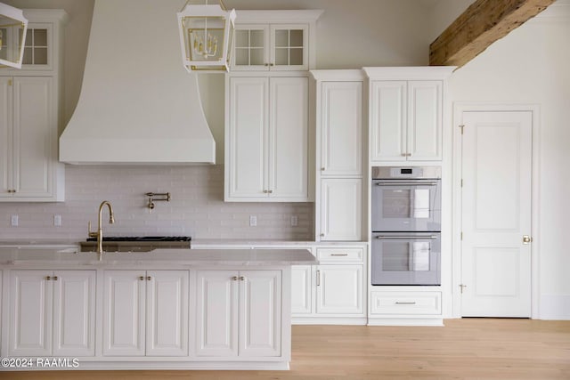 kitchen featuring white cabinetry, backsplash, stainless steel double oven, and custom range hood