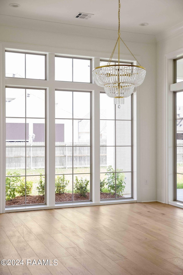 unfurnished dining area with plenty of natural light, light wood-type flooring, and an inviting chandelier