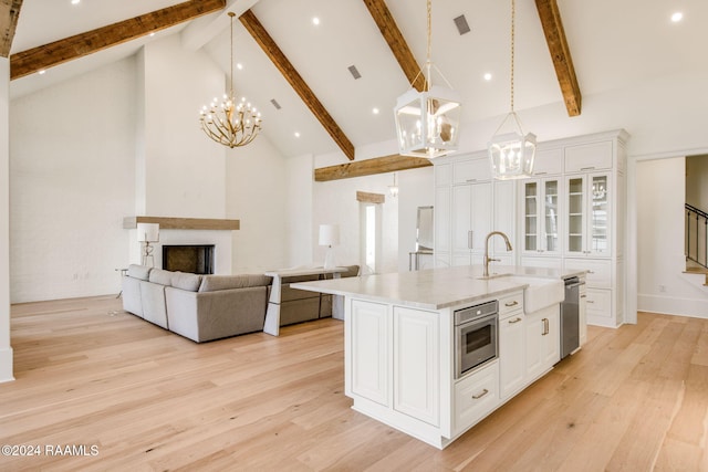 kitchen featuring white cabinetry, hanging light fixtures, high vaulted ceiling, stainless steel dishwasher, and a center island with sink