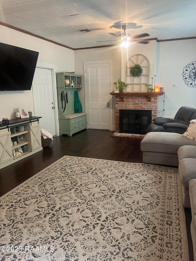 living room featuring ceiling fan, dark hardwood / wood-style flooring, crown molding, and a brick fireplace