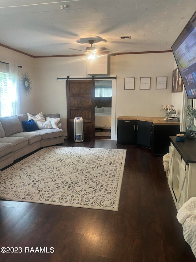 living room with ornamental molding, ceiling fan, a barn door, and dark wood-type flooring