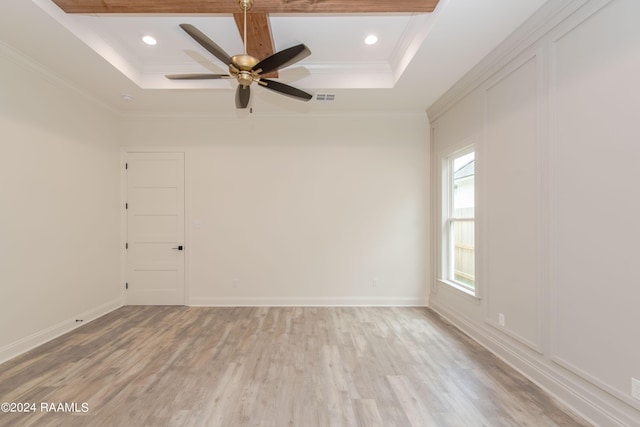 empty room featuring ceiling fan, light wood-type flooring, a tray ceiling, and crown molding