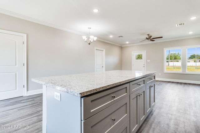 kitchen with decorative light fixtures, light stone countertops, a center island, and crown molding