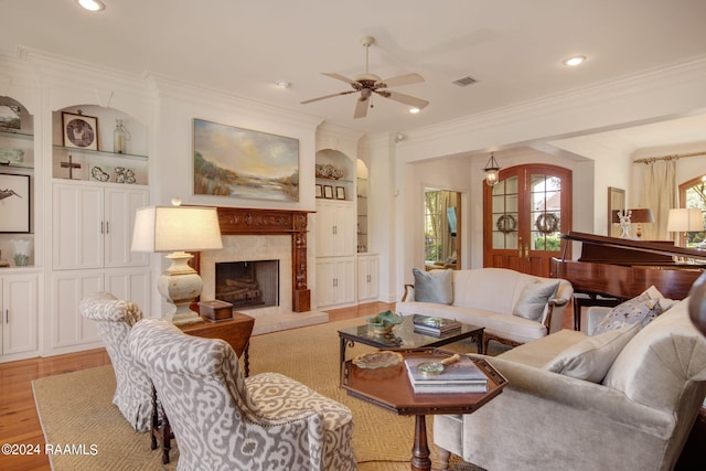 living room with built in features, ceiling fan, crown molding, and light wood-type flooring