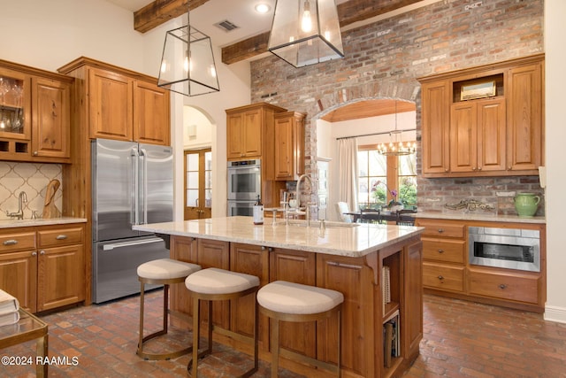 kitchen with decorative light fixtures, stainless steel appliances, backsplash, a kitchen island with sink, and beamed ceiling