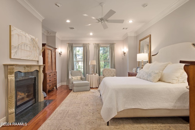 bedroom featuring wood-type flooring, ceiling fan, a fireplace, and crown molding