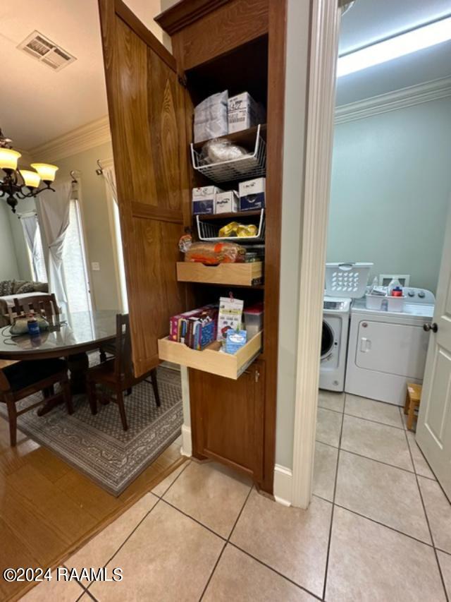 interior space with washing machine and clothes dryer, crown molding, light tile patterned floors, and an inviting chandelier