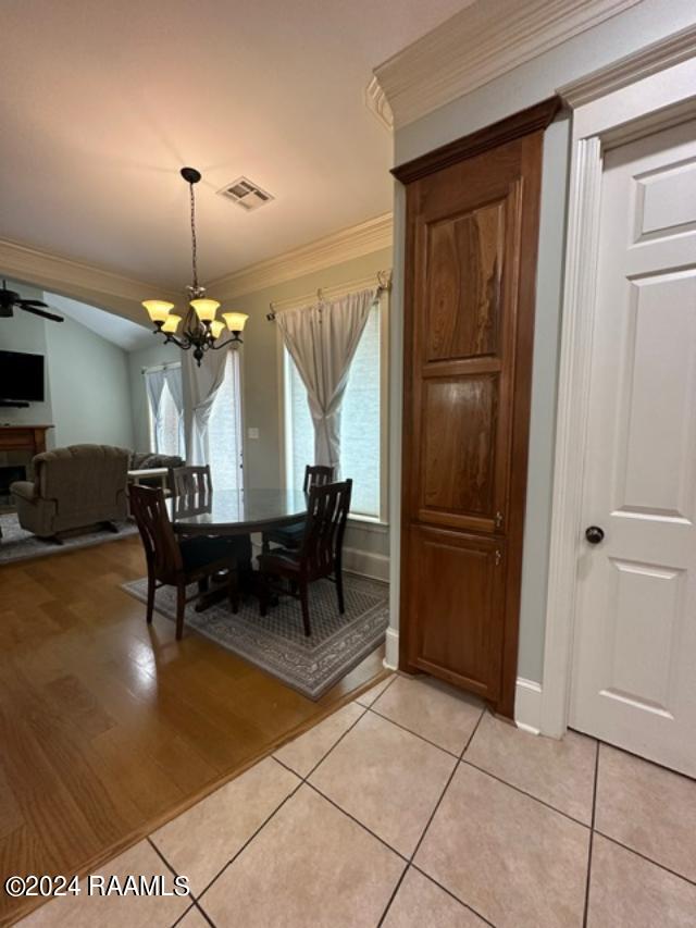 dining space with light tile patterned floors, ceiling fan with notable chandelier, and crown molding