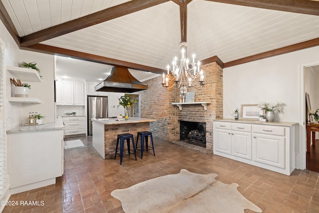 living room with brick wall, beam ceiling, a notable chandelier, and a fireplace