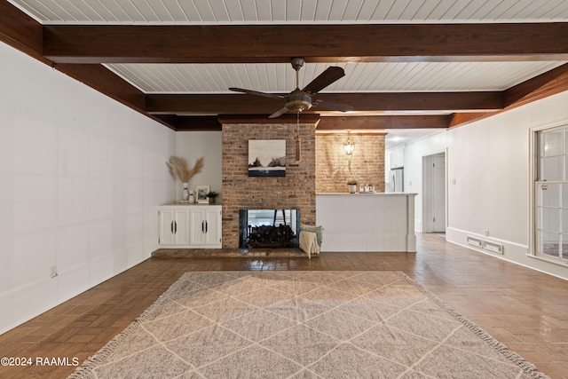 unfurnished living room with a fireplace, beam ceiling, ceiling fan, and brick wall