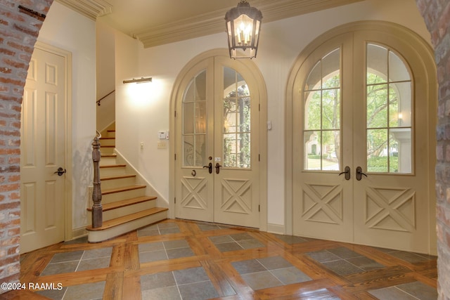 entryway featuring brick wall, french doors, ornamental molding, and a notable chandelier