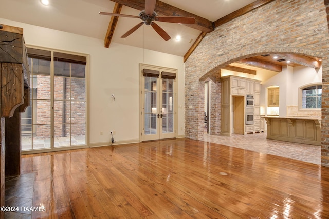 unfurnished living room with french doors, ceiling fan, light wood-type flooring, beamed ceiling, and a healthy amount of sunlight