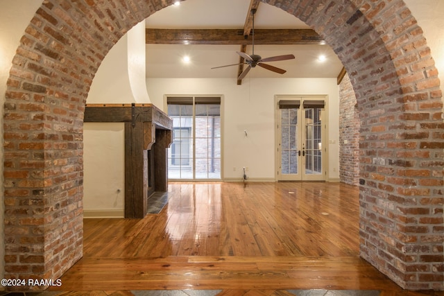 unfurnished living room with ceiling fan, french doors, beamed ceiling, brick wall, and hardwood / wood-style flooring