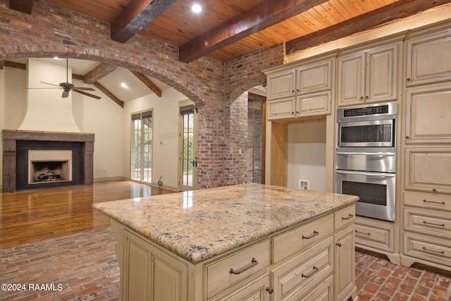 kitchen featuring a large fireplace, stainless steel double oven, light stone counters, cream cabinets, and a kitchen island