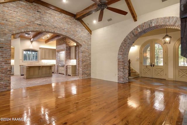 unfurnished living room with beam ceiling, french doors, high vaulted ceiling, and light hardwood / wood-style flooring