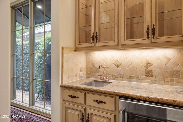 bar with decorative backsplash, light stone counters, sink, and beverage cooler