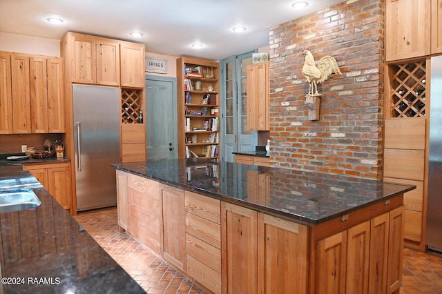 kitchen featuring sink, stainless steel built in fridge, dark stone countertops, and light brown cabinetry