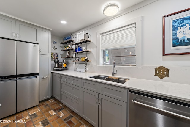 kitchen with light stone countertops, gray cabinetry, stainless steel appliances, sink, and tasteful backsplash