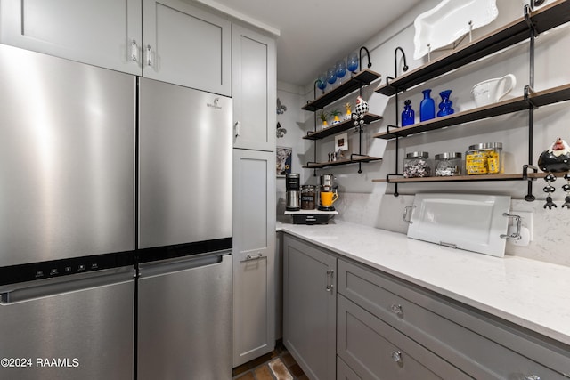 kitchen featuring light stone countertops, stainless steel refrigerator, and gray cabinetry