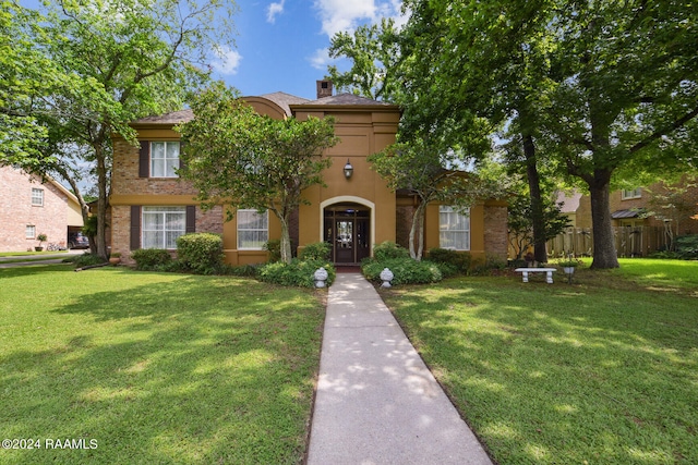 mediterranean / spanish home featuring brick siding, fence, stucco siding, a chimney, and a front yard