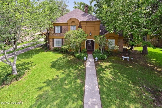 view of front of home featuring brick siding, roof with shingles, a chimney, stucco siding, and a front lawn