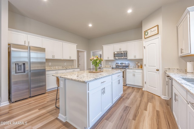 kitchen featuring a center island, stainless steel appliances, white cabinetry, and light wood-type flooring