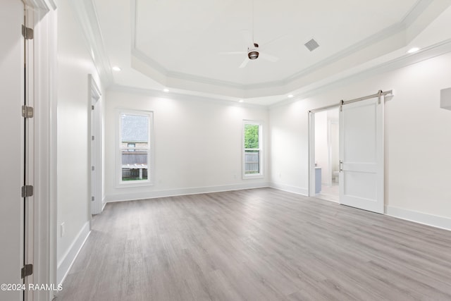 empty room featuring a barn door, a raised ceiling, light hardwood / wood-style floors, and ornamental molding