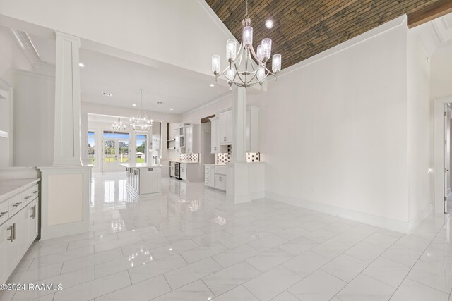 unfurnished dining area featuring a notable chandelier, ornate columns, marble finish floor, high vaulted ceiling, and ornamental molding