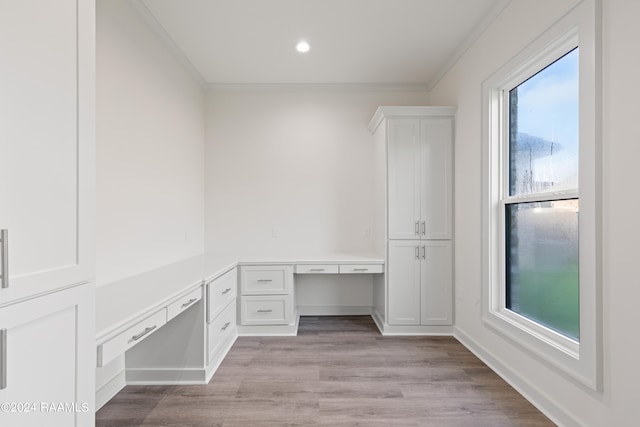 unfurnished office with light wood-type flooring, built in desk, and crown molding