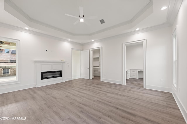 unfurnished living room with light hardwood / wood-style flooring, a raised ceiling, and crown molding