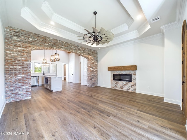 unfurnished living room featuring a tray ceiling, crown molding, brick wall, and hardwood / wood-style flooring