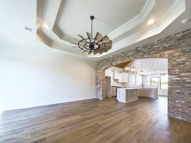 unfurnished living room with a raised ceiling, crown molding, sink, and dark hardwood / wood-style floors