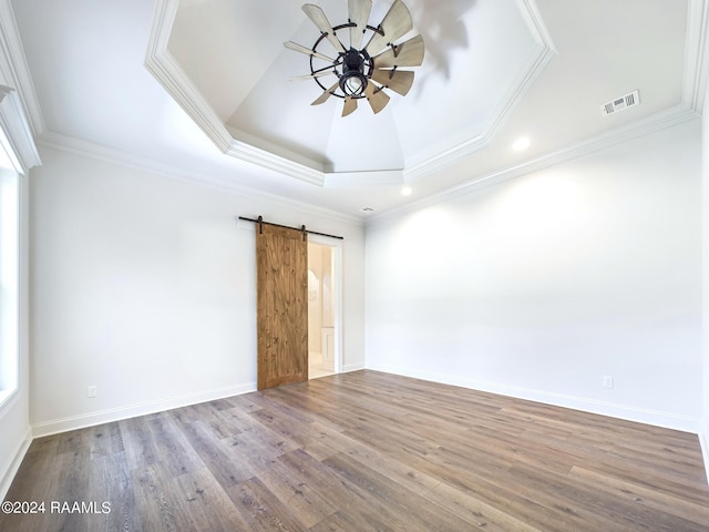 spare room with a raised ceiling, crown molding, light hardwood / wood-style flooring, ceiling fan, and a barn door