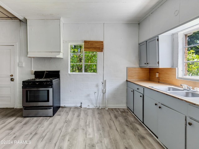 kitchen with light hardwood / wood-style floors, stainless steel gas range oven, custom range hood, gray cabinetry, and sink