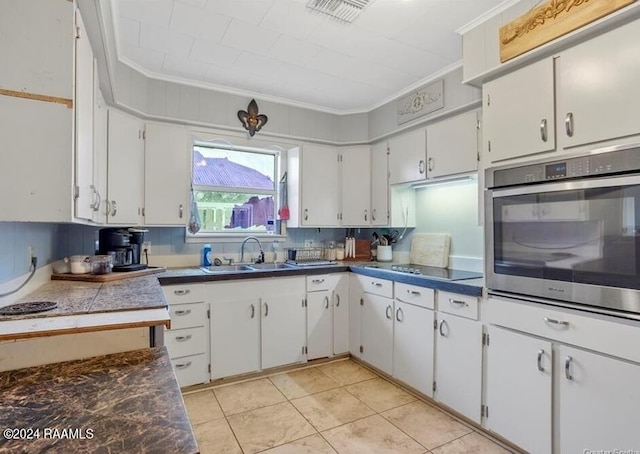 kitchen with tasteful backsplash, white cabinetry, stainless steel oven, sink, and light tile floors