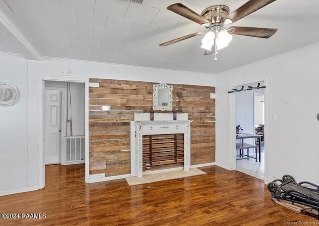 unfurnished living room featuring wooden walls, ornamental molding, ceiling fan, and dark hardwood / wood-style floors