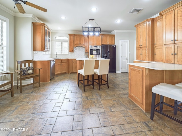 kitchen featuring appliances with stainless steel finishes, a kitchen bar, decorative backsplash, a kitchen island, and ornamental molding